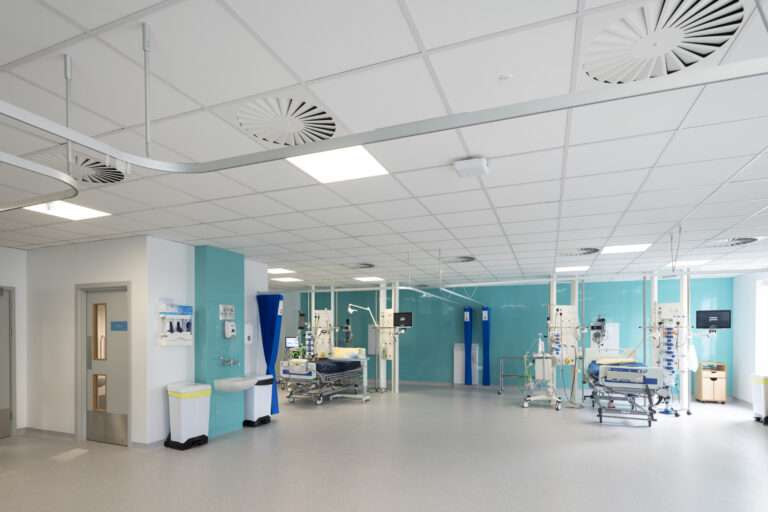 A high dependency ward room, featuring a hospital bed and a lot of medical monitoring equipment. In the foreground there is a hand washing station. The rear wall is a light blue colour.