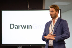 The Darwin Group CEO, Richard Pierce, stood in front of a large display screen, giving a presentation.