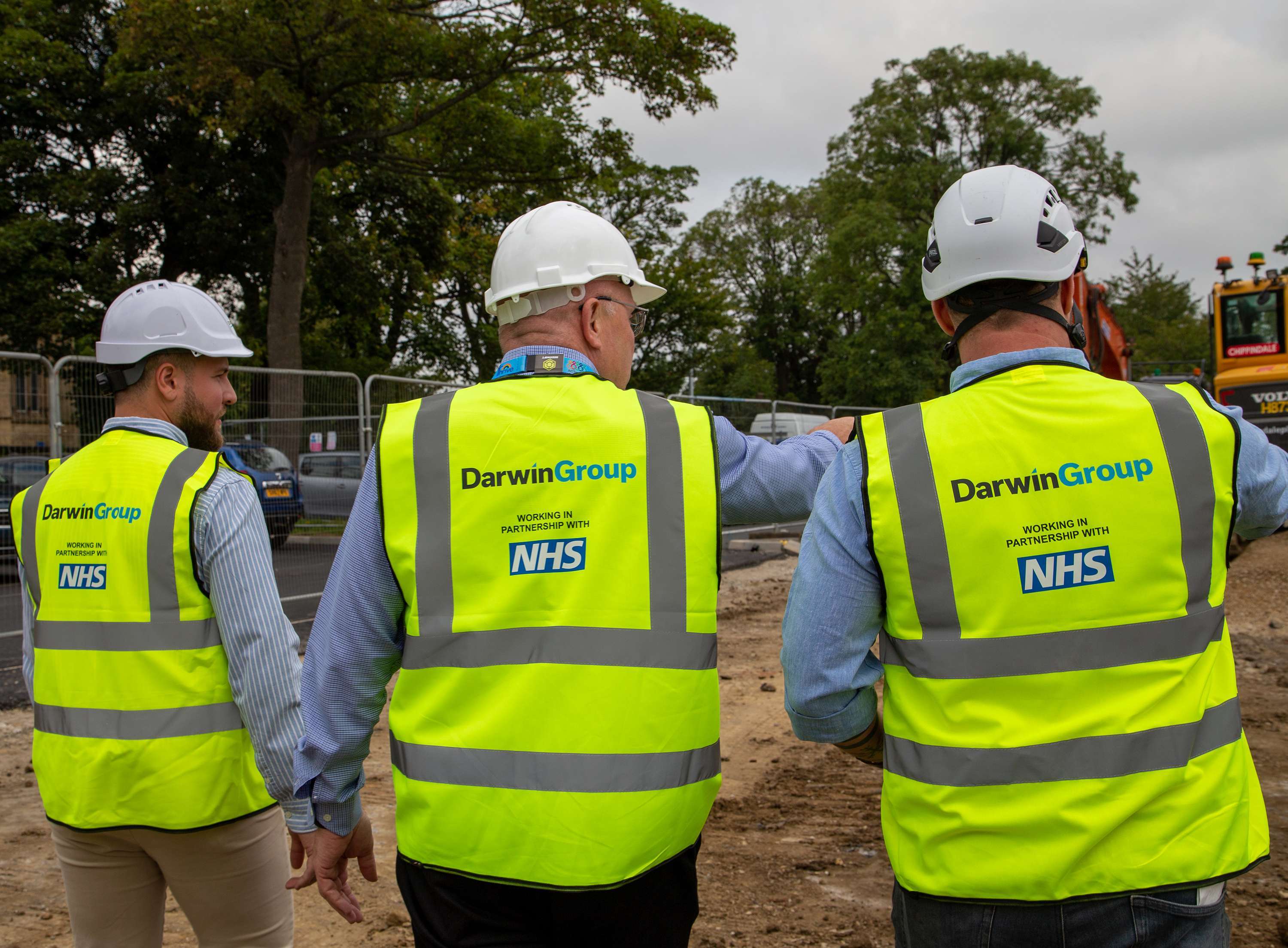 Three men in Darwin Group branded PPE, pictured from behind as they look out over a building site.