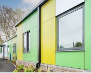 External view of a building that features green and yellow cladding, regularly punctuated with windows that have grey frames.