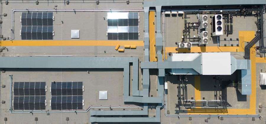 An overhead view of a hospital building's roof, showing a range of plant machinery. This includes four photovoltaic solar panel arrays and a number of HVAC and air-conditioning units.